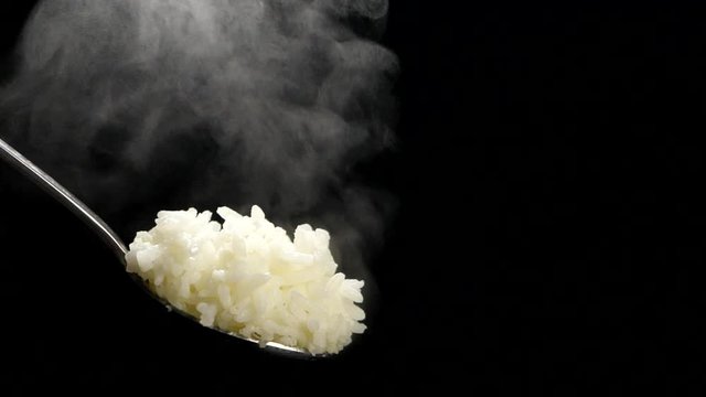 Rice on spoon with steam in slow motion on black background