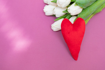A bouquet of white tulips and a red velvet heart on a pink background-the concept of Valentine's Day.