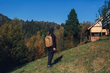 girl photographer with backpack stands on slope and view nature in mountains in fall.