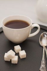 Morning tea in a white cup with sugar cubes on a black tray.