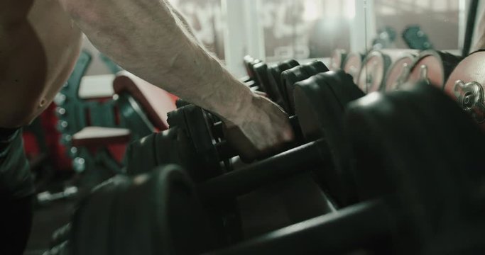 Male bodybuilder picks up free weights inside indoor gym