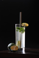 Lemonade soda in Tall glass with bamboo straw with mint leaves and fresh cut lemons in the background