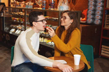 Cute couple having breakfast in cafe together. Woman feeding her boyfriend with biscuit. Romantic couple drinking coffee