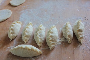 Closeup of raw homemade pastries before baking on wooden background with white flour. Cooking traditional ukrainian pies, patties. Flat lay. Copy space