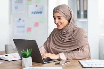 Happy islamic woman in hijab working on laptop in office
