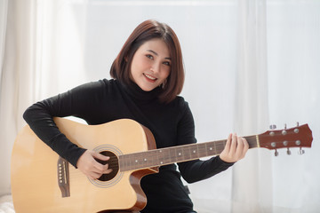 Portrait of young asian woman playing a guitar.