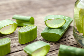 Aloe Vera gel cream for skin and body care. Aloe pulp slices in a glass jar and leaves on a wooden table. Cosmetic lotion.