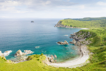 Aerial view of beach in beautiful bay on green coast with rocks and turquoise sea. Sunny summer seaside landscape in Asia. Gamov Peninsula in Primorsky Krai, Far East, Russia