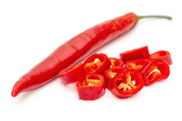 Whole red chili pepper with slices of red chili pepper on white.