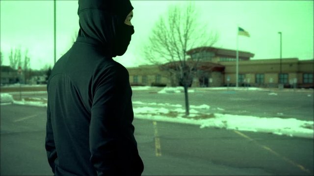 CCTV or security camera footage of a man who is a killer or terrorist outside a school, hospital or some public building branishing a large knife