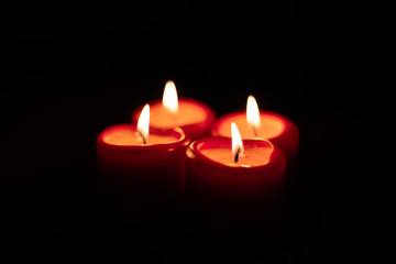 Xmas Christmas season symbol. Four candles symbolize advent weeks. Detail of four red candles burning, isolated with black surrounding.
