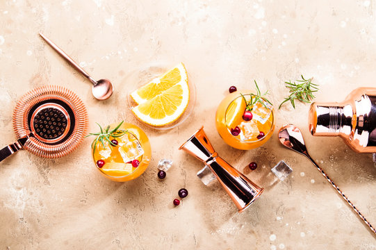Orange Cranberry Rosemary and Vodka cocktail, copper bar tools, beige background, hard light, top view
