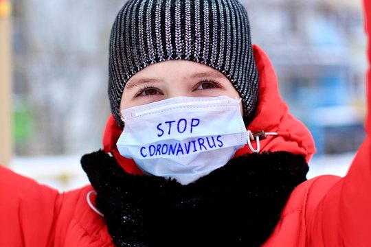 Teenage girl wearing protective medical mask with stop coronavirus text against transmissible infectious diseases and as protection against new virus 2019-nCoV in public places as children playground. - Powered by Adobe