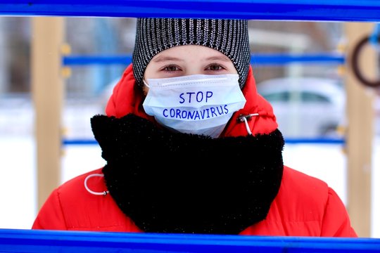 Teenage girl wearing protective medical mask with stop coronavirus text against transmissible infectious diseases and as protection against new virus 2019-nCoV in public places as children playground. - Powered by Adobe