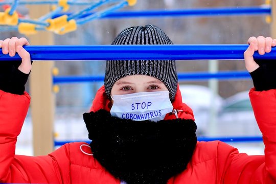 Teenage girl wearing protective medical mask with stop coronavirus text against transmissible infectious diseases and as protection against new virus 2019-nCoV in public places as children playground. - Powered by Adobe