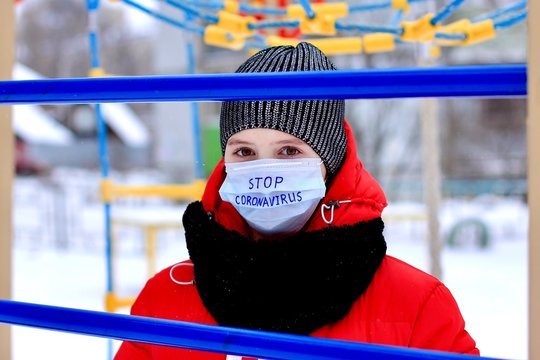 Teenage girl wearing protective medical mask with stop coronavirus text against transmissible infectious diseases and as protection against new virus 2019-nCoV in public places as children playground. - Powered by Adobe