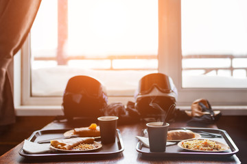 Hot coffee and cup of tea with pancakes and jam on a salver. Quick lunch of two skiers on mountain ski resort. Casual dinner of a snowboarder. Two helmets with goggles on table in restaurant.