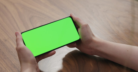 Young woman sitting at a table and using a smartphone with horizontal green screen