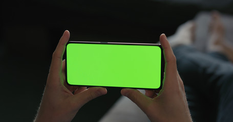 man use smartphone with green screen while lying on a couch