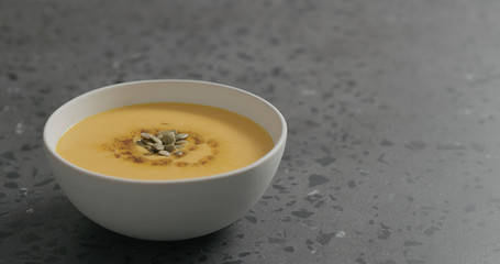 pumpkin cream soup in white bowl on terrazzo countertop