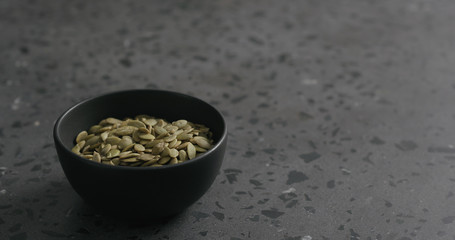 pumpkin seeds in black bowl on terrazzo countertop with copy space