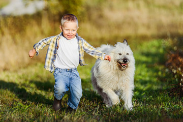 Happy smiling blond boy running with dog friend on farm