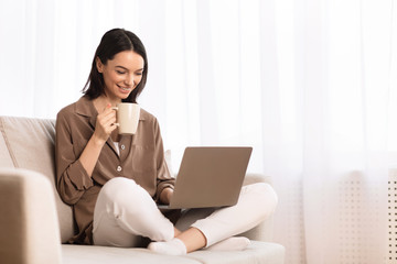 Naklejka premium Young woman using laptop sitting on the couch