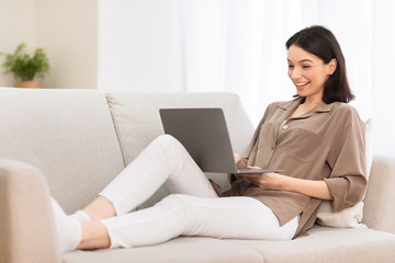 Young girl working on laptop online at couch