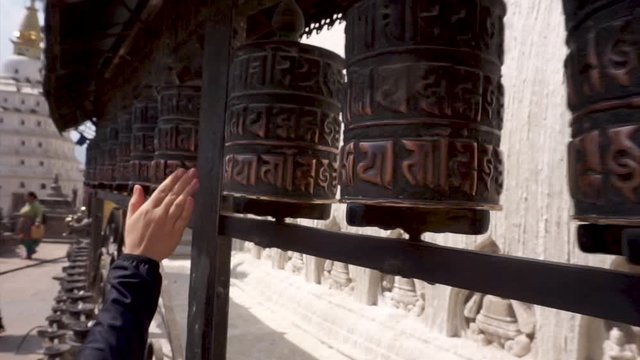 A woman is rolling prayer wheels at Swayambhunath Stupa (Monkey Temple) in Kathmandu Nepal with the mantra Om Mani Padme Hum