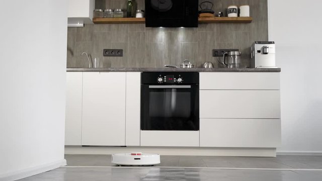 In a stylish modern kitchen is cleaning. The automatic robot vacuum cleaner moves along its trajectory. Elements of a smart home make life easier for people