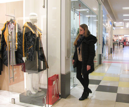 young woman in a shopping center look at maniken through the glass