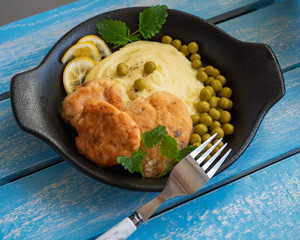 Breakfast on a black plate with mashed potatoes and fish cutlets with green peas