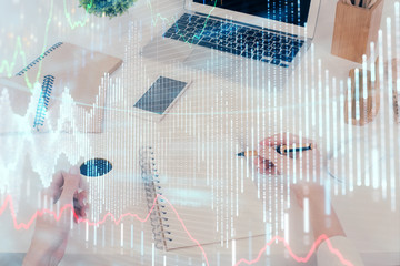 Hands writing information about stock market in notepad. Forex chart holograms in front. Concept of research. Multi exposure