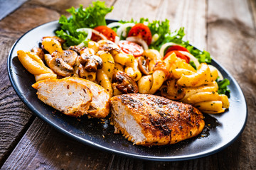Roast chicken breast with pasta and vegetables on wooden background