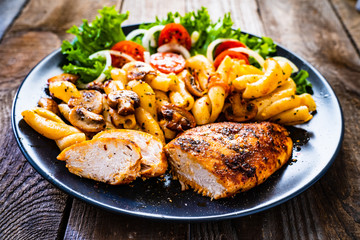 Roast chicken breast with pasta and vegetables on wooden background