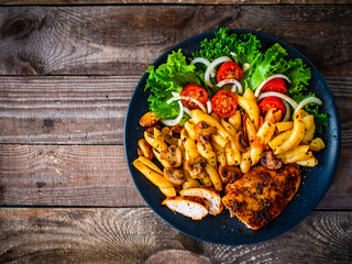 Roast chicken breast with pasta and vegetables on wooden background