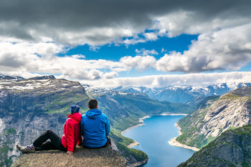 Fototapeta premium Travel concept. The couple sitting on a cliff over a lake, Trolltunga, Norway. Amazing nature view. Artistic picture. Beauty world. The feeling of complete freedom