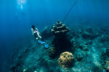 Young woman free diver glides with fins near underwater temple. Freediving in ocean
