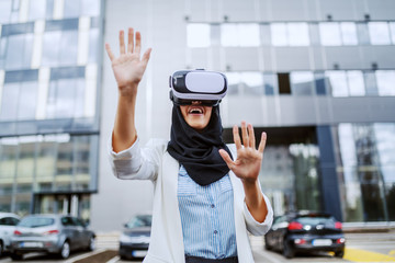 Attractive young muslim businesswoman with scarf on head using vr goggles for virtual presentation. Millennial generation.