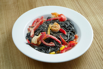 Stylish black pasta with cuttlefish ink, vegetables, cream sauce and shrimp in a white plate on a wooden background. Fancy Italian Black Spaghetti