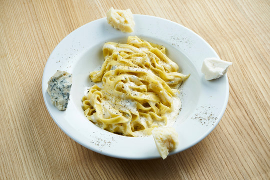 Italian pasta with four types of cheese in a white plate on a wooden background. Tagliatale in cream cheese sauce. Close up view on tasty food