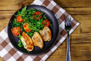 Fried chicken breast with salad of fresh arugula and cherry tomatoes on wooden table. Top view