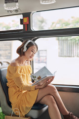 Young woman reading book while moving in the modern tram, happy passenger at the public transport
