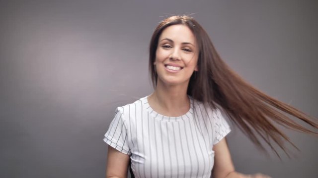 Portrait of adorable lady making long hair flyaway and turns on grey background
