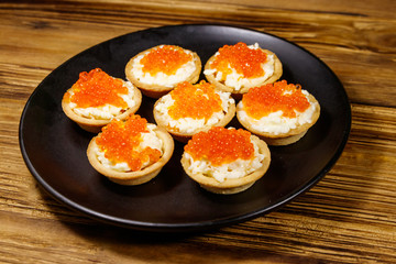 Tartlets with red caviar and soft cheese on a wooden table