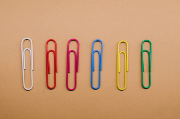 paper clips of different colors lying at the same distance from each other on a brown background