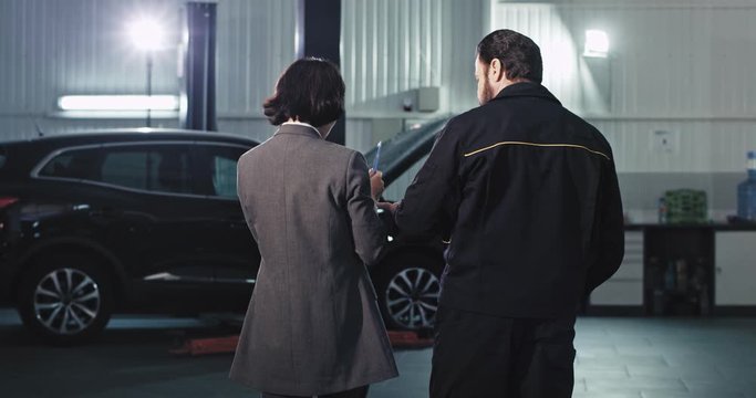 Business woman in a suit and the main mechanic from the garage have a friendly conversation in the auto service center they smiling and feeling great