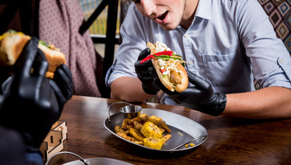 Two hungry young men eating a hot dogs in cafe. Restaurant