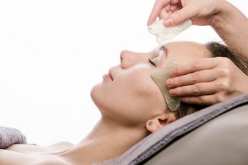 Young woman having a gua sha face massage at asian beauty clinic. Side view