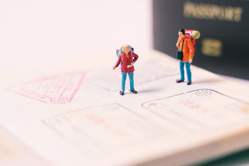 Miniature people figures with backpack walking and standing on passport page with immigration...